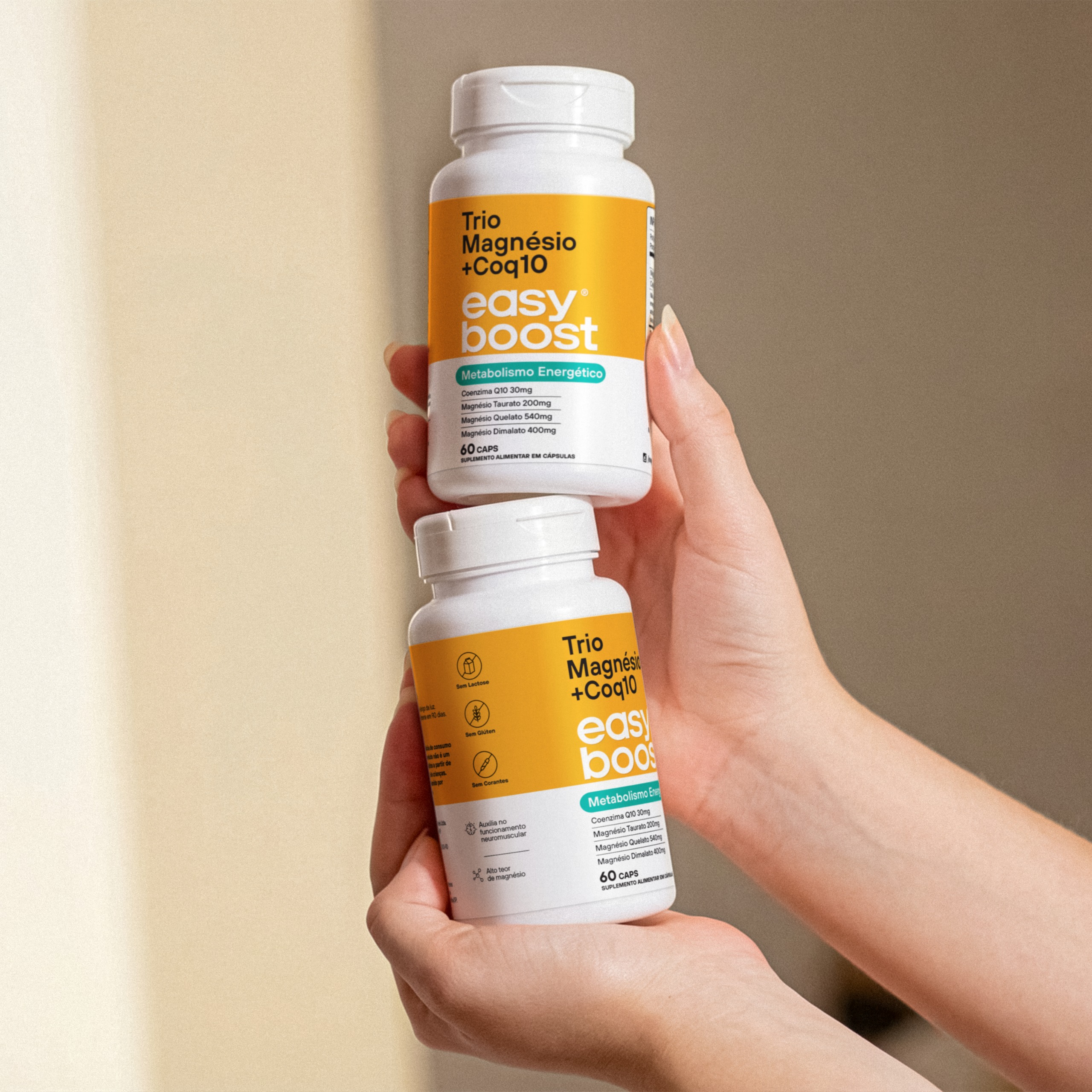 Duas embalagens do suplemento Trio Magnésio + CoQ10 Easy Boost, metabolismo energético, 60 cápsulas, sendo seguradas por duas mãos.